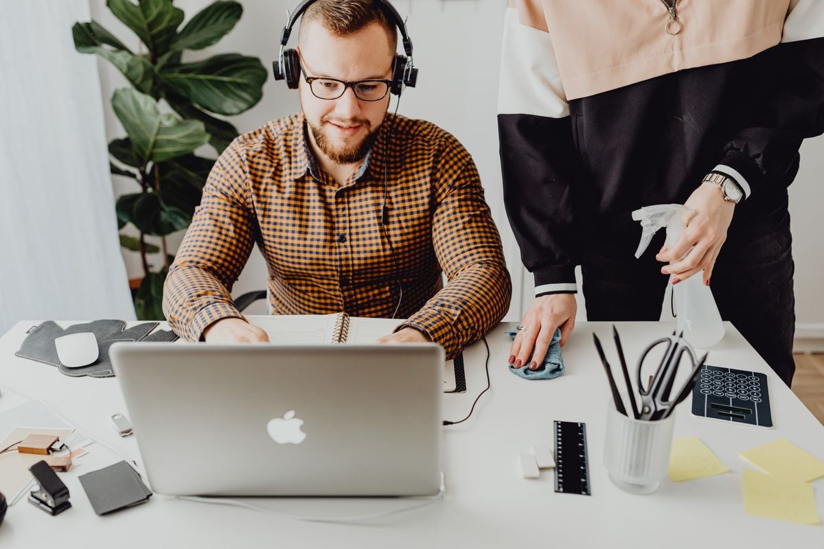 A professional cleaner sanitizing a desk in a bright modern office while an employee works nearby